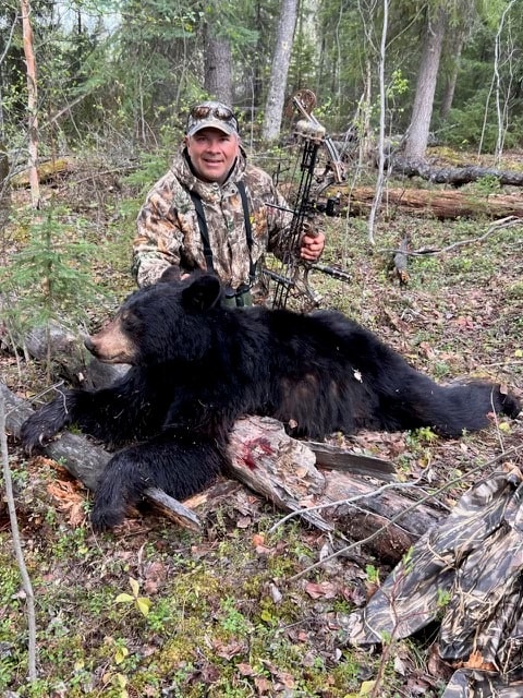 Bowhunter with harvested black bear in Saskatchewan forest