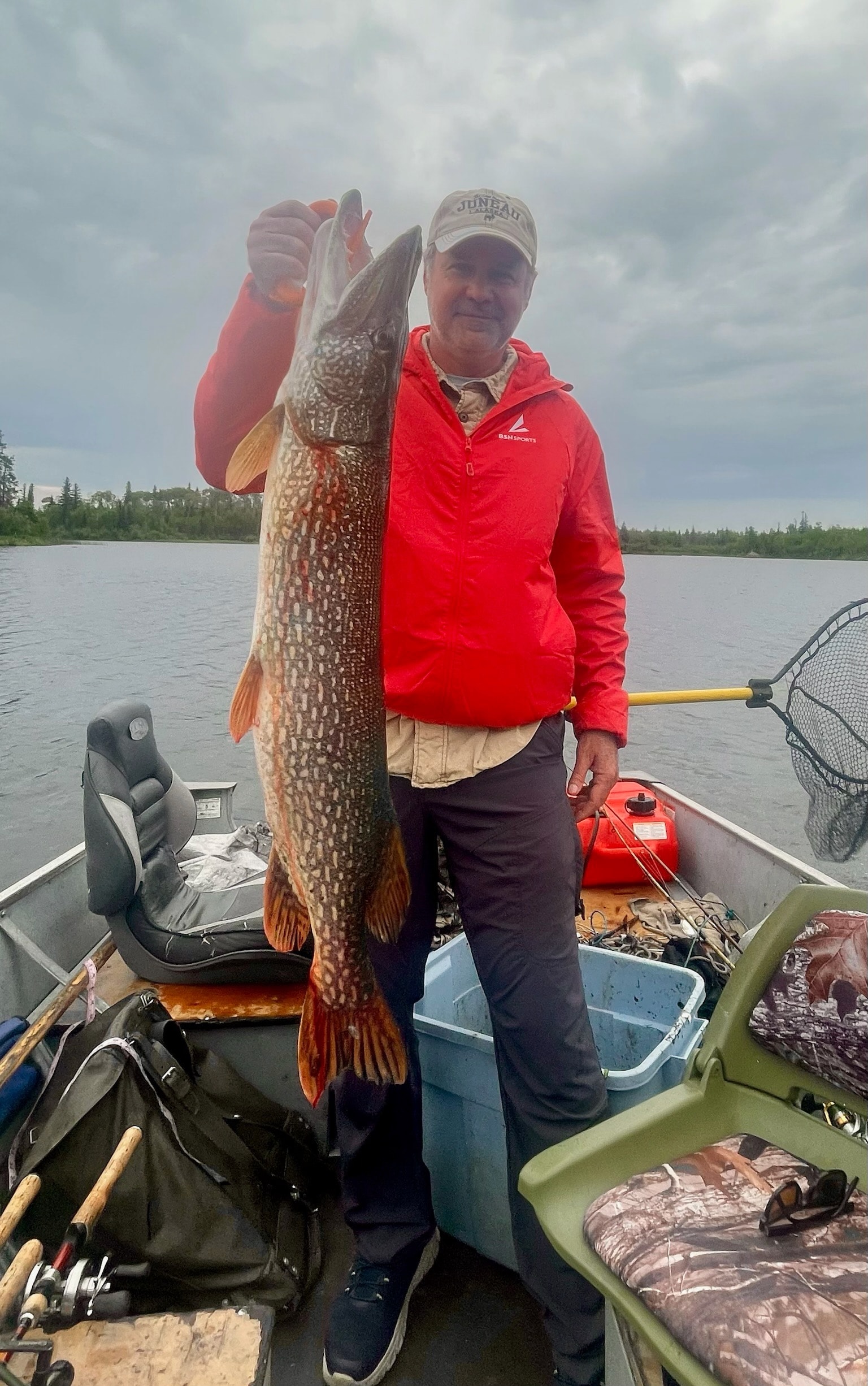 Man in red jacket holding a large Northern Pike in a boat