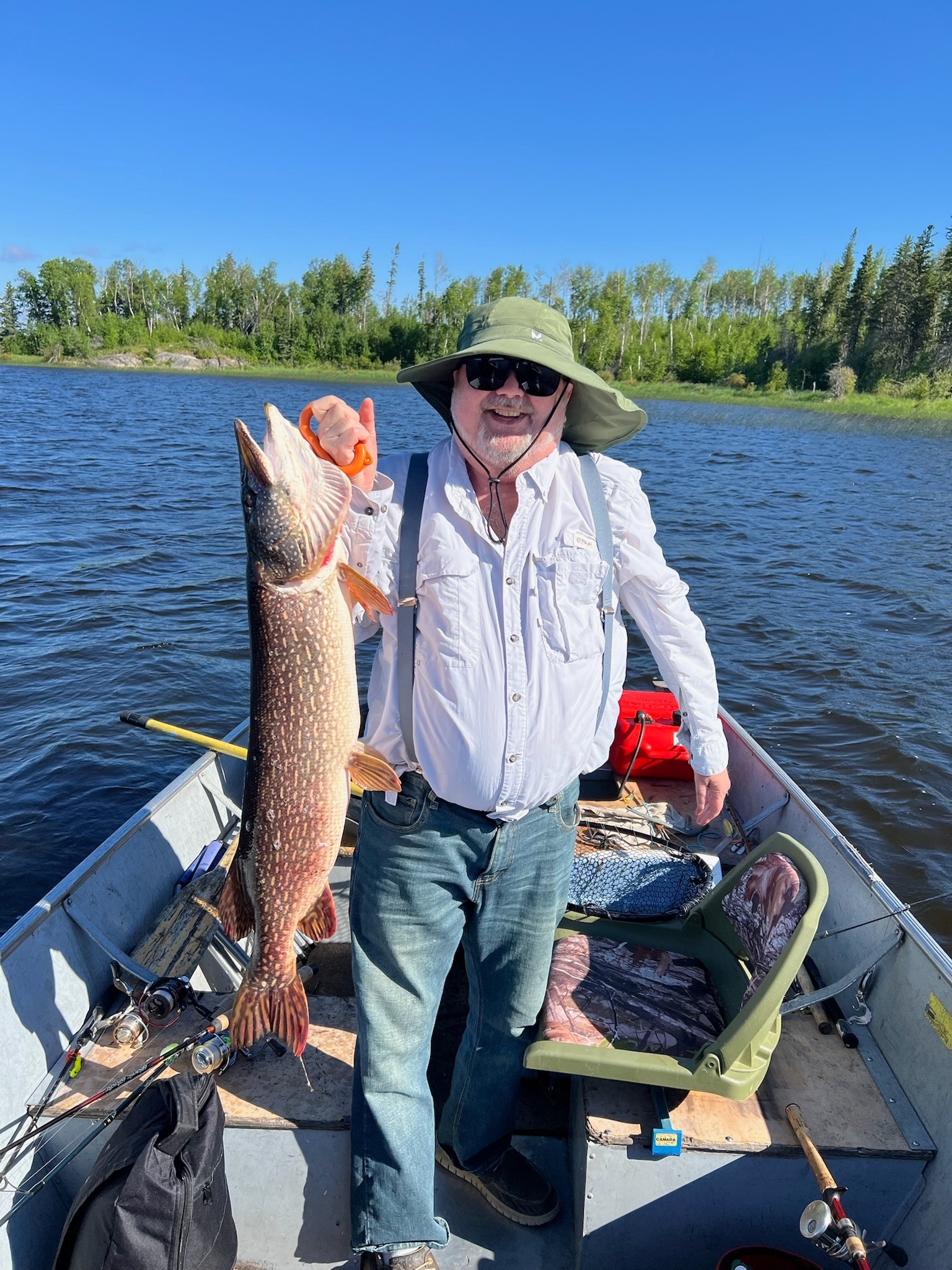 Man in green hat holding a large Northern Pike in a boat