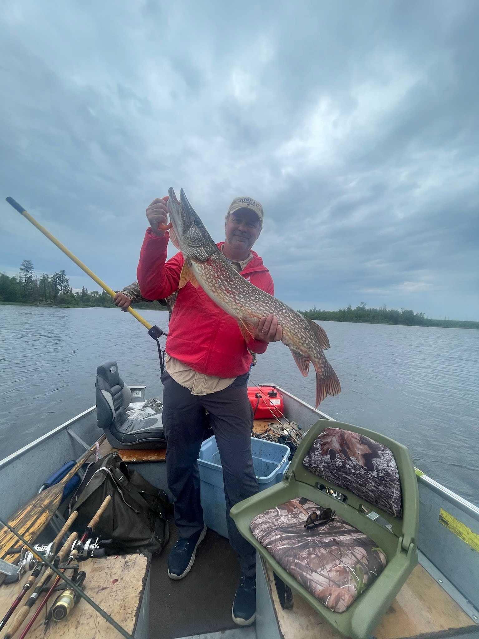 Man in red jacket holding a large pike with both hands in a boat