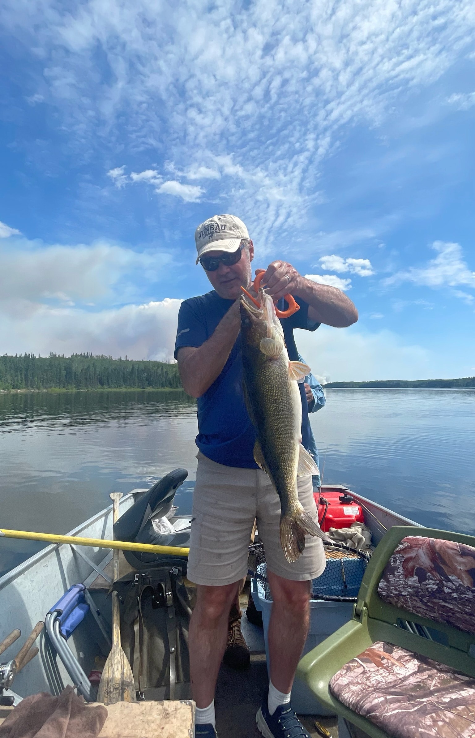 Man in blue shirt holding a walleye on a calm lake