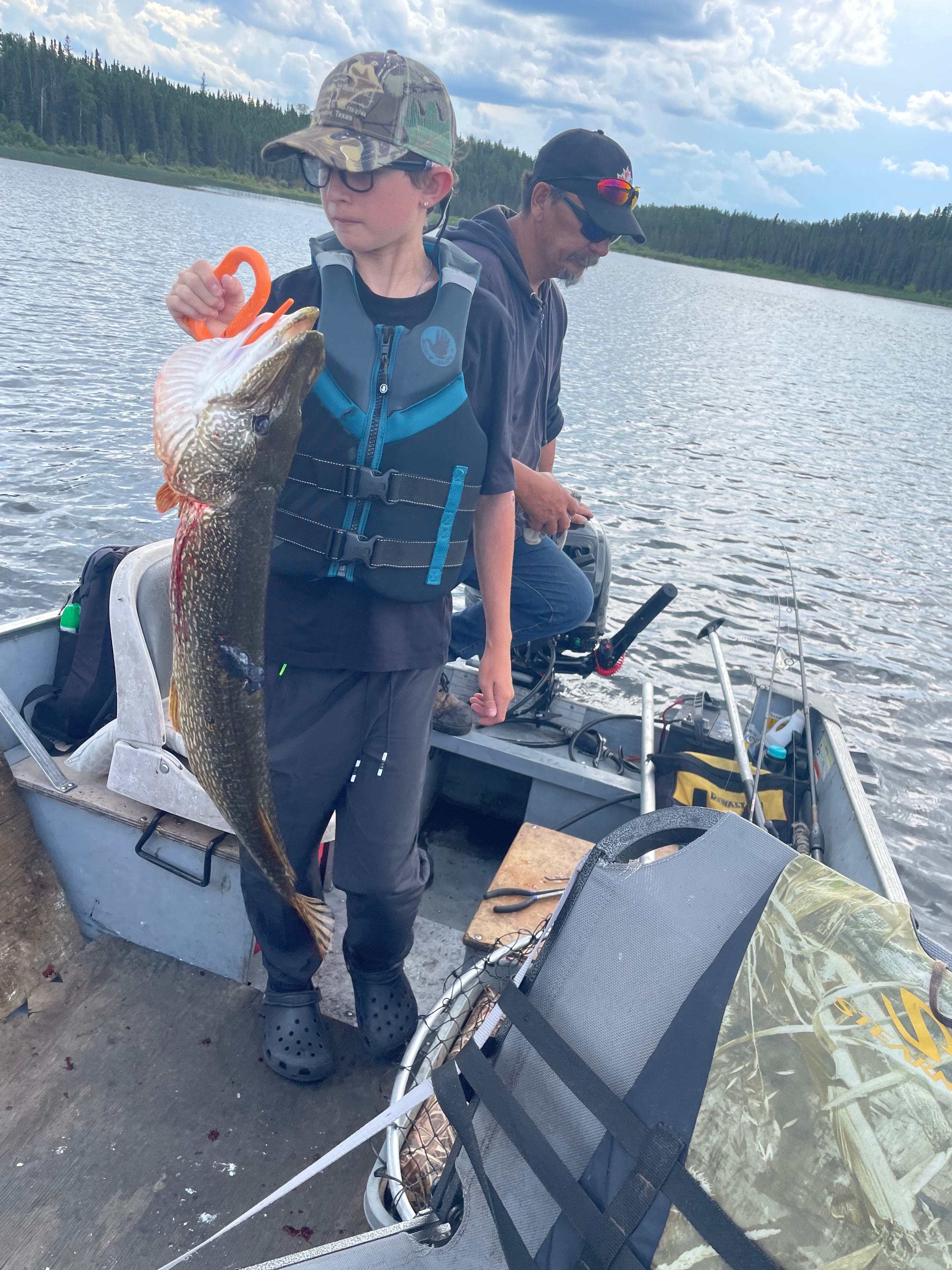 Young boy in life jacket holding a large pike in a boat