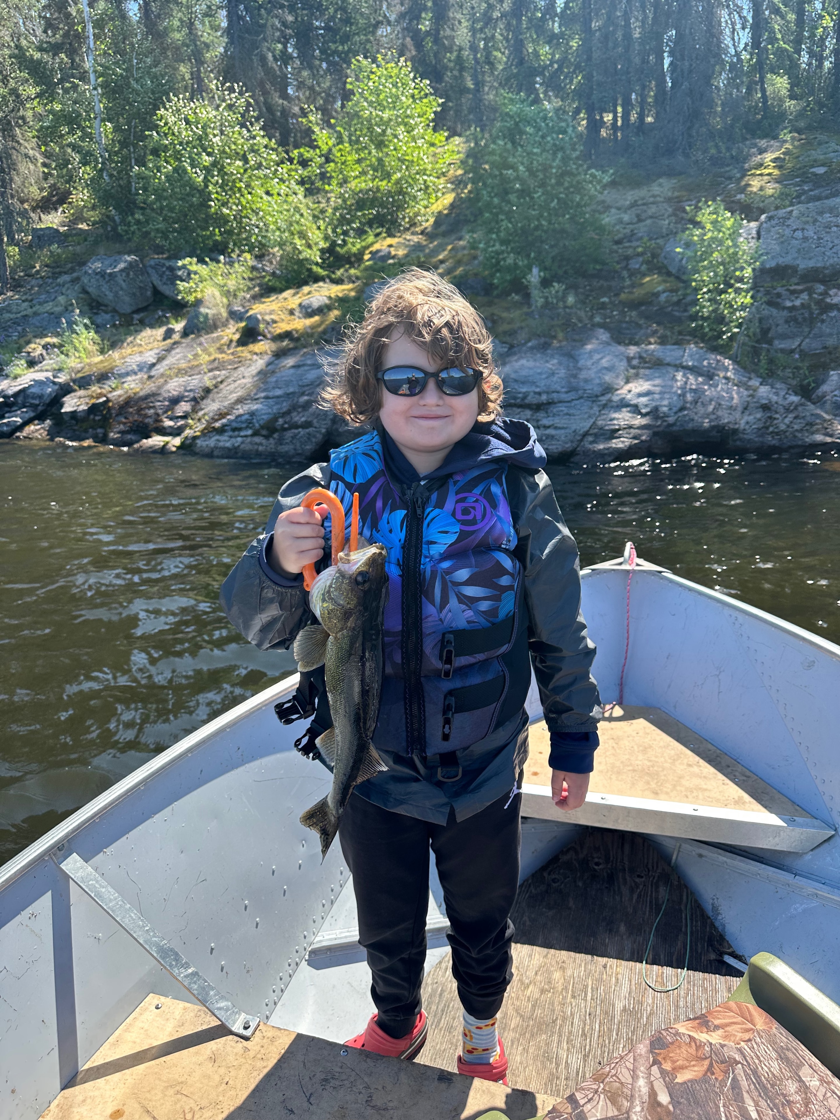 Boy in life jacket holding a Northern Pike with a lip gripper in a Black Bear Island Lodge boat