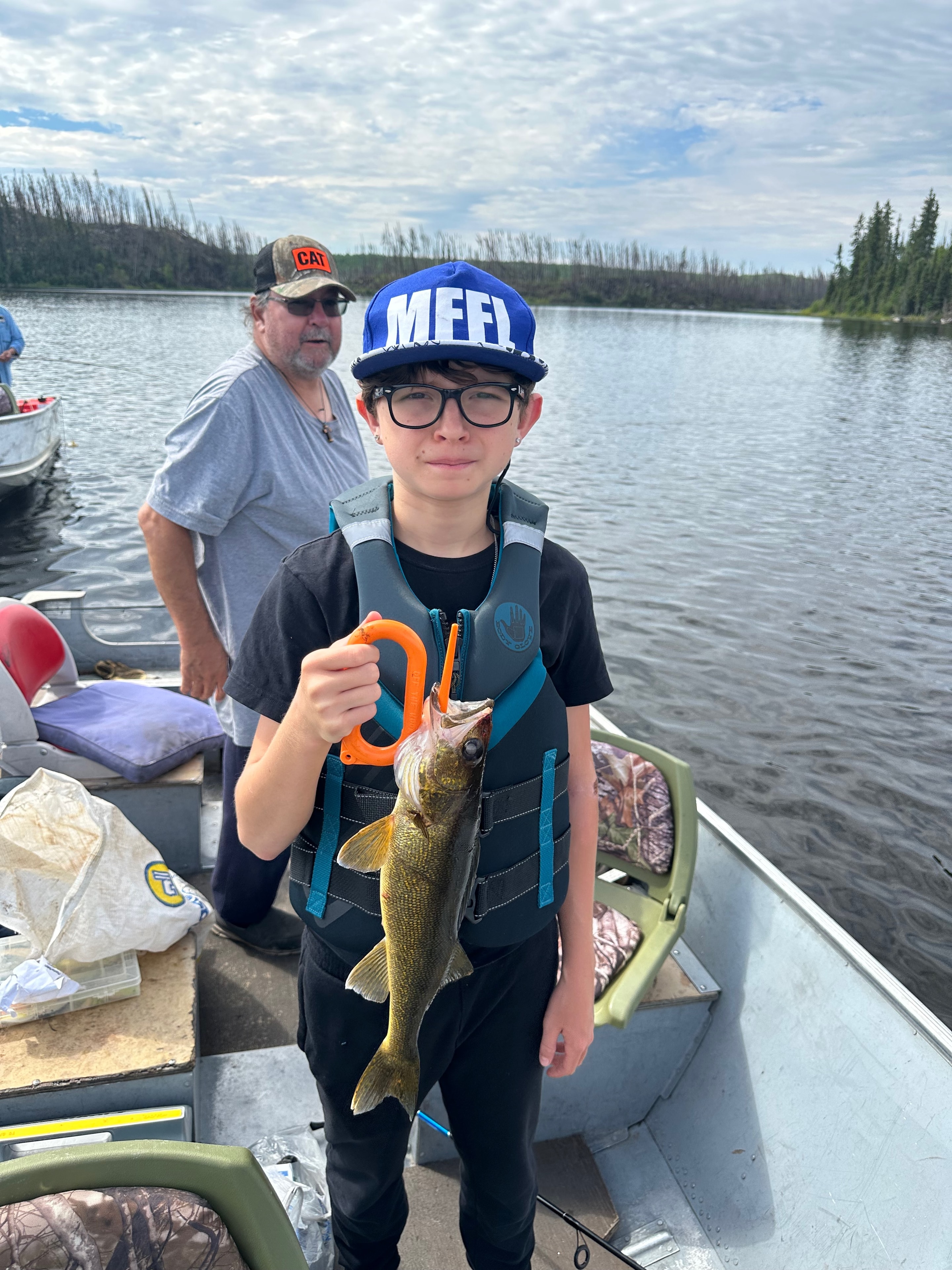 Young boy in Dallas Cowboys hoodie holding a Northern Pike with a lip gripper in a boat on a sunny lake