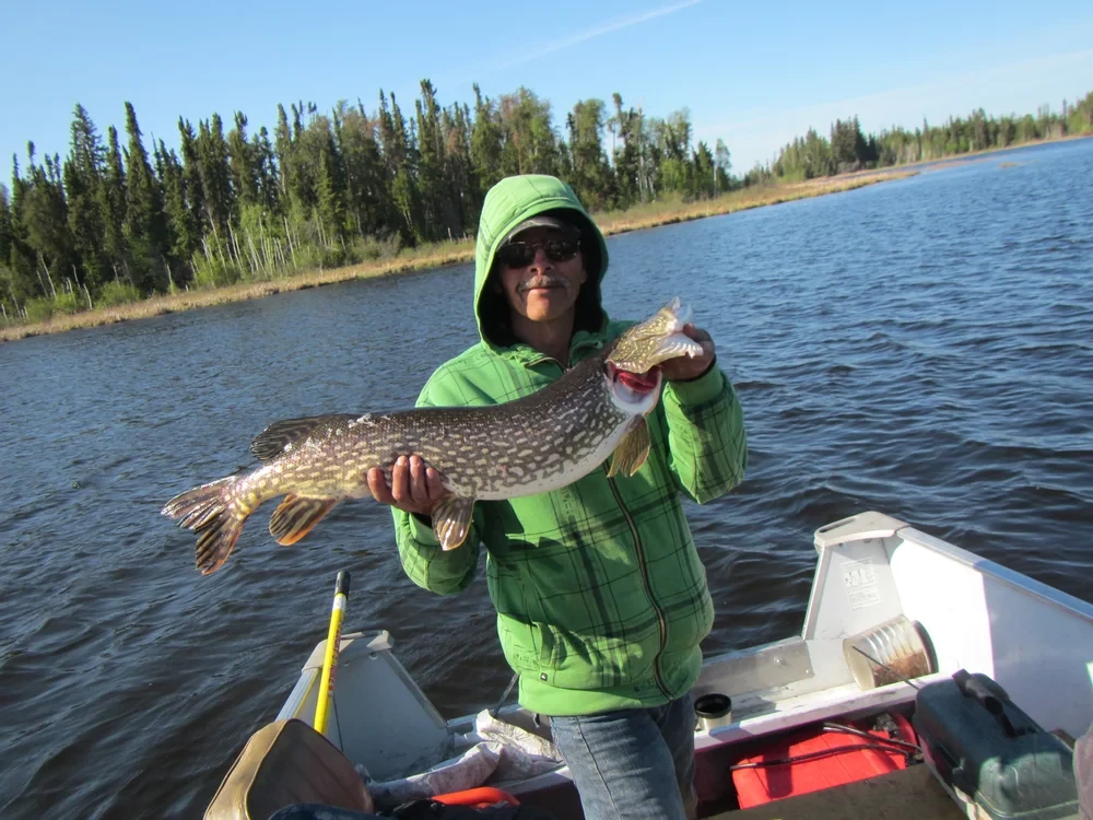 Man in cowboy hat and red bandana holding a big pike, dramatic stormy sky