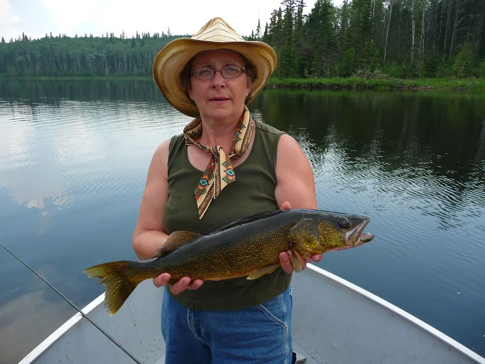 Angler with a large pike, wilderness lake and forest backdrop