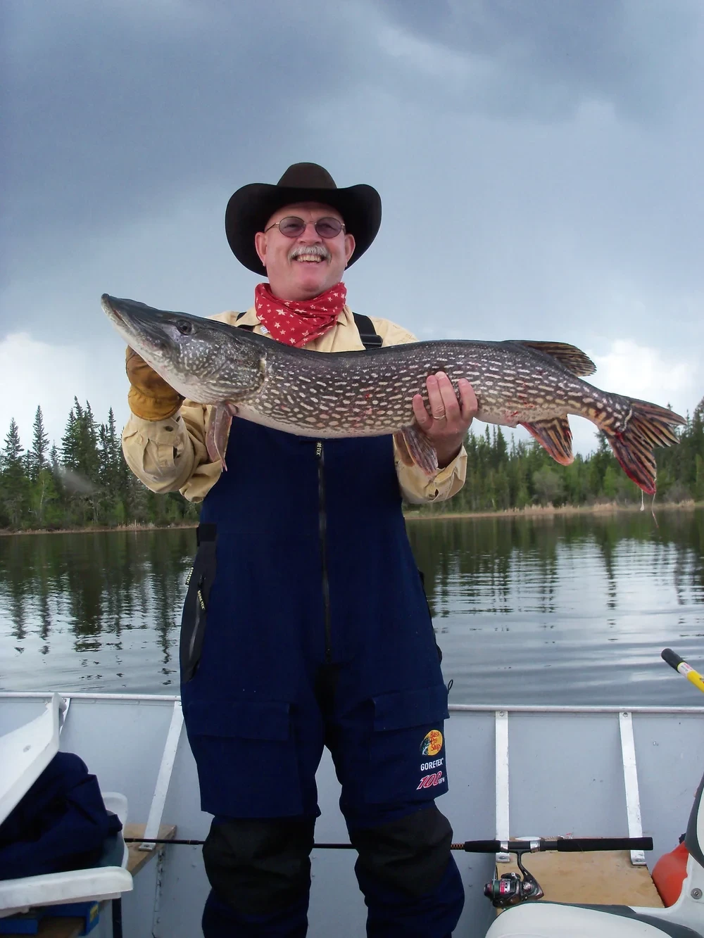 Man holding two Northern Pike at once, sunny blue sky, wide river view