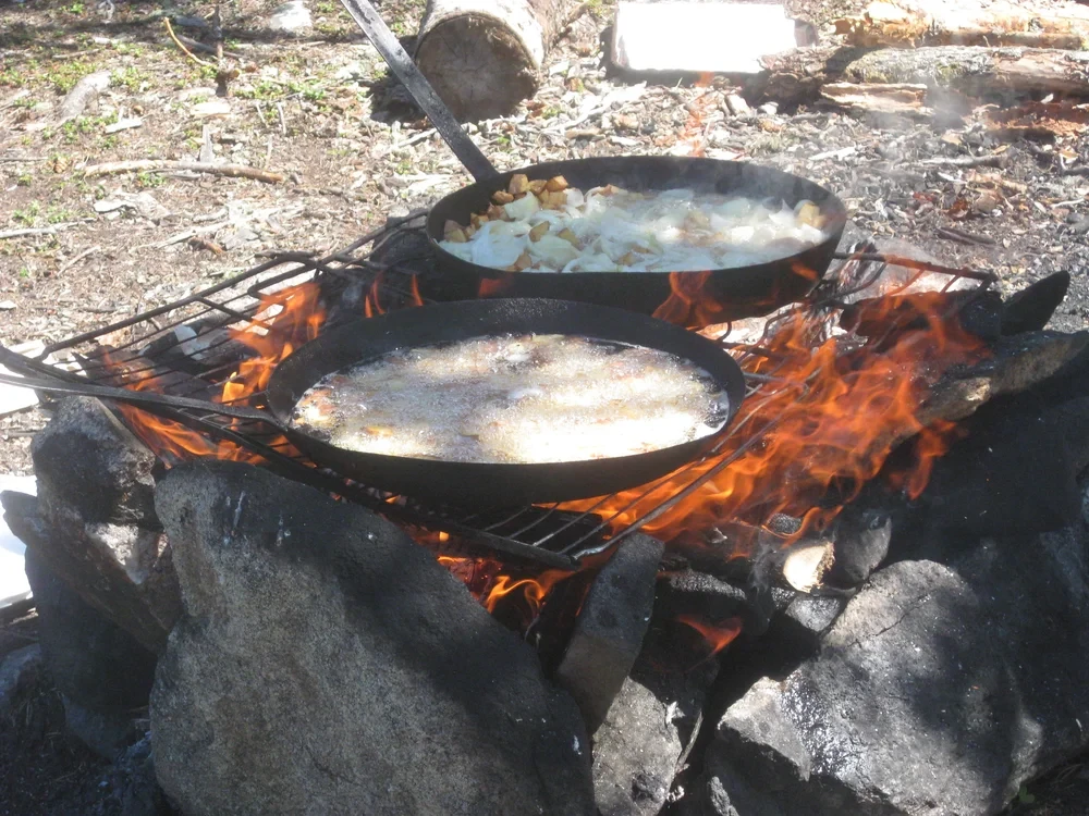 Shore lunch — two cast-iron skillets over an open campfire