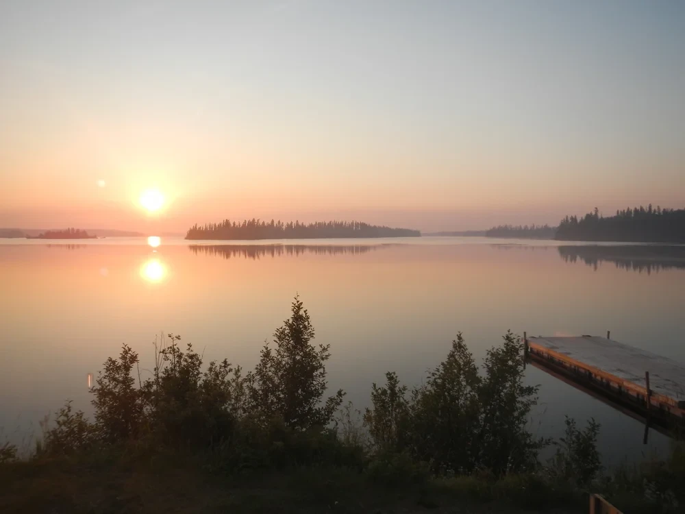 Sunrise over the calm lake with dock and island silhouettes