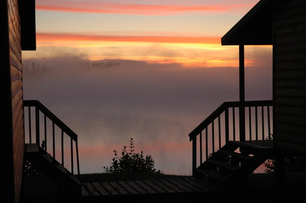 Fiery sunrise framed between two cabin porches with fog over the lake