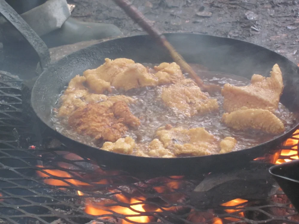Shore lunch — walleye fillets frying in a cast iron pan over open flames