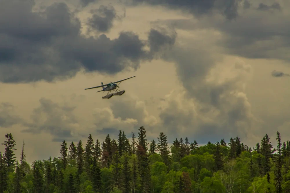 Floatplane flying over the boreal forest treeline under dramatic cloudy skies
