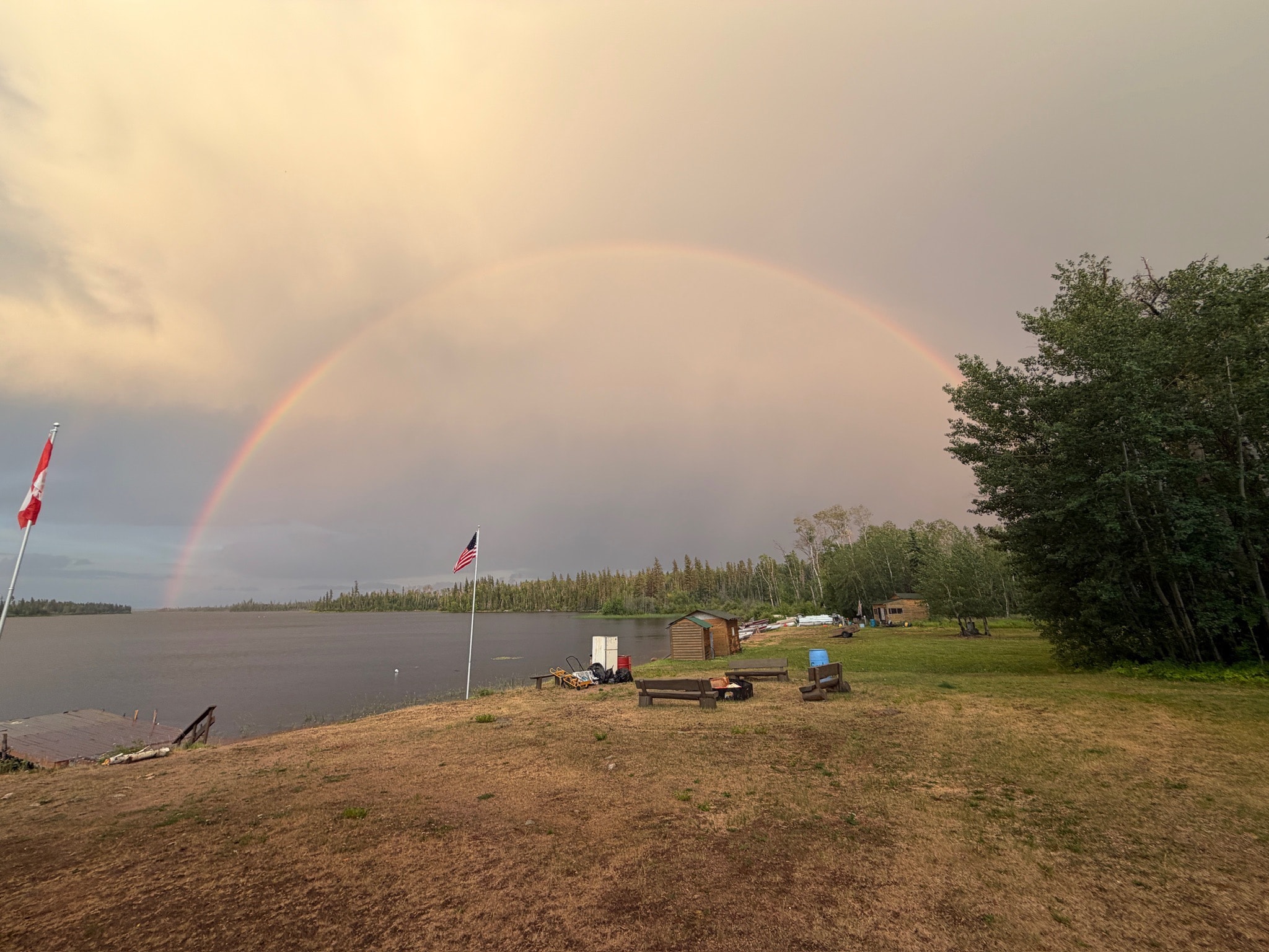 Full rainbow arching over Black Bear Island Lodge grounds with Canadian and US flags