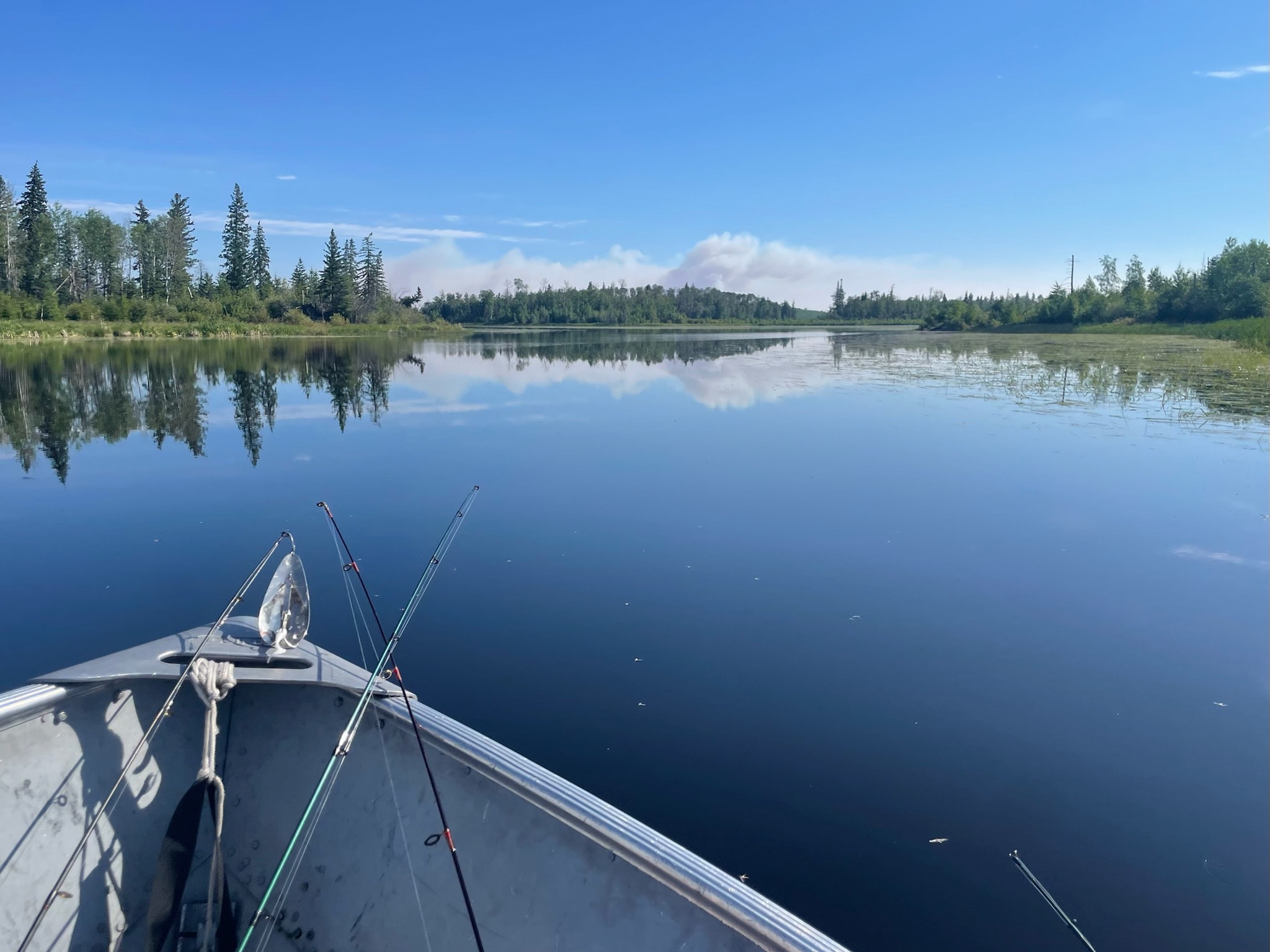 Fishing rods on the bow of a boat on a mirror-calm lake