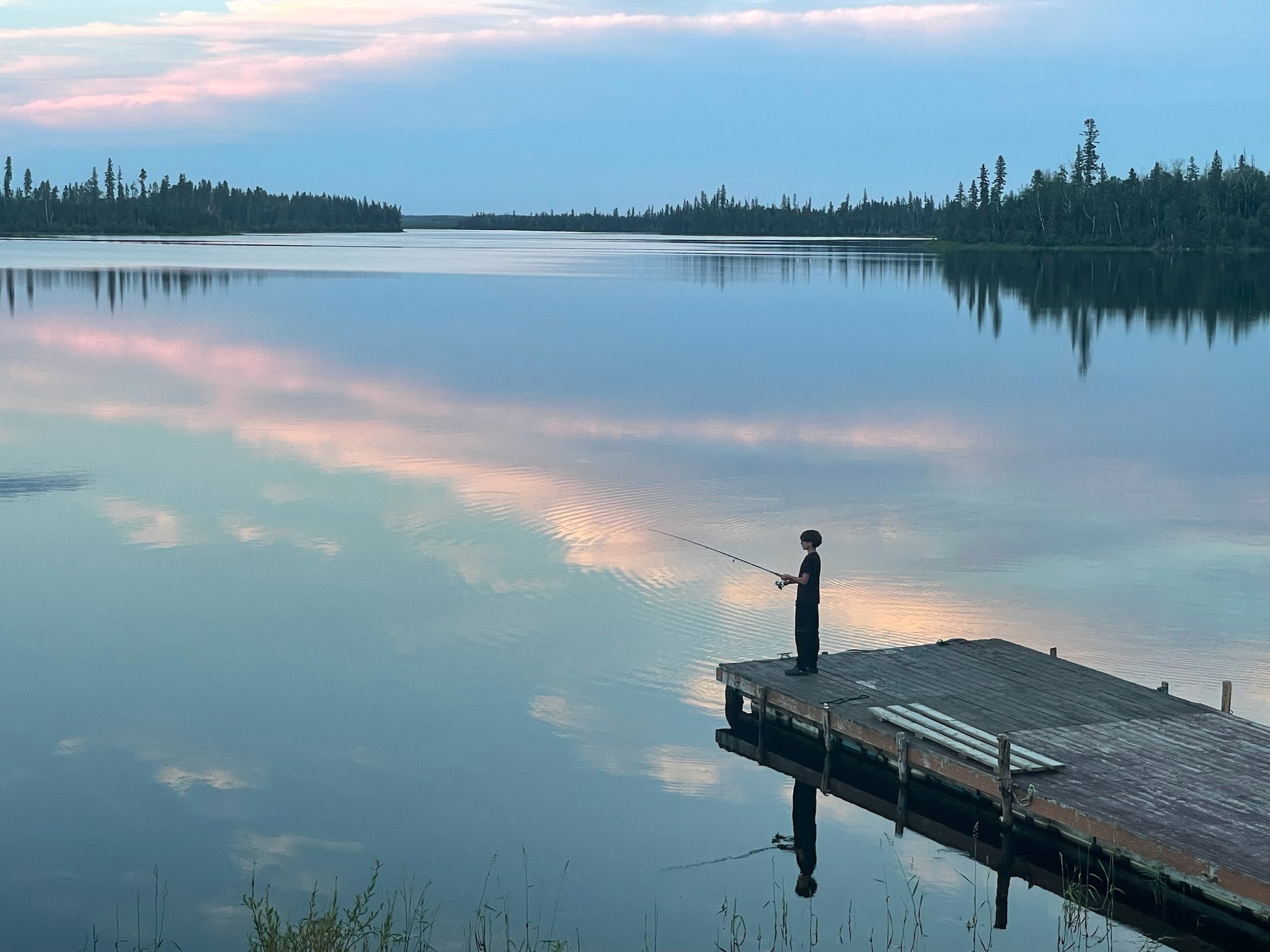 Child fishing from the dock at dusk with pastel sky reflecting on the lake