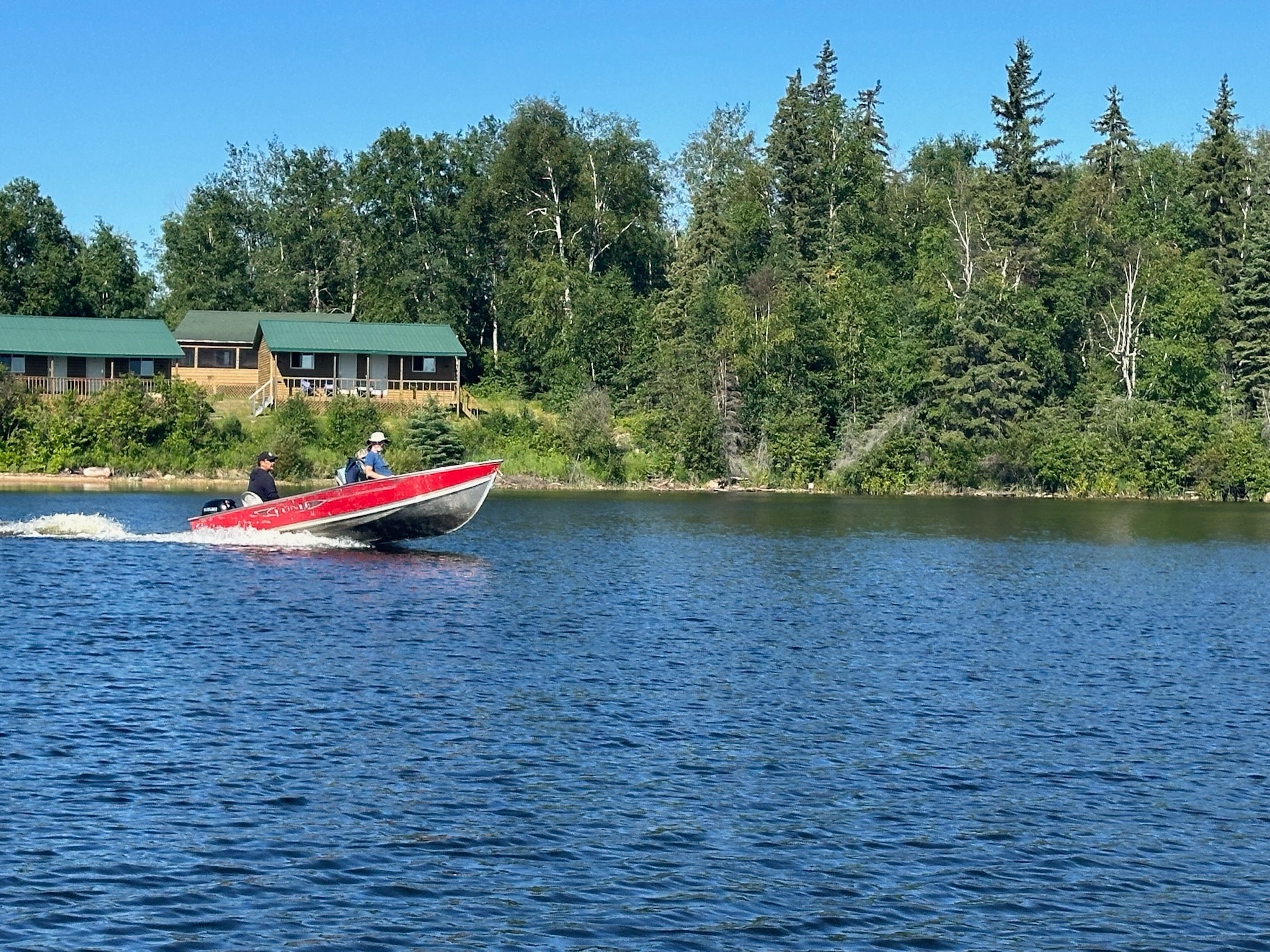 Red fishing boat speeding past Black Bear Island Lodge cabins on a sunny day