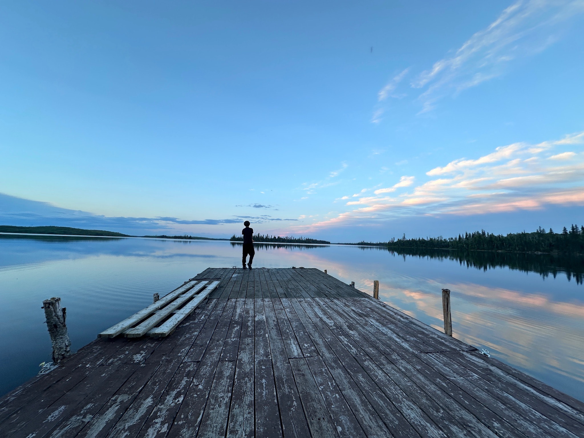Silhouette of person standing on dock at twilight with pastel sky and calm lake