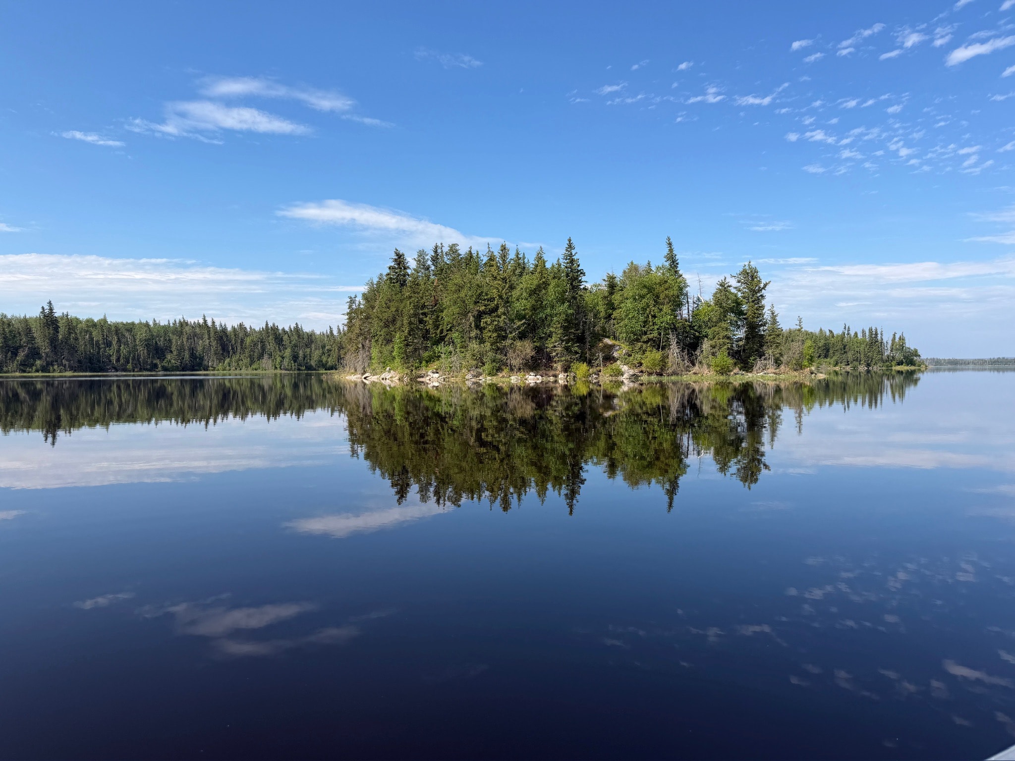 Forested island perfectly mirrored in glassy calm lake under blue sky