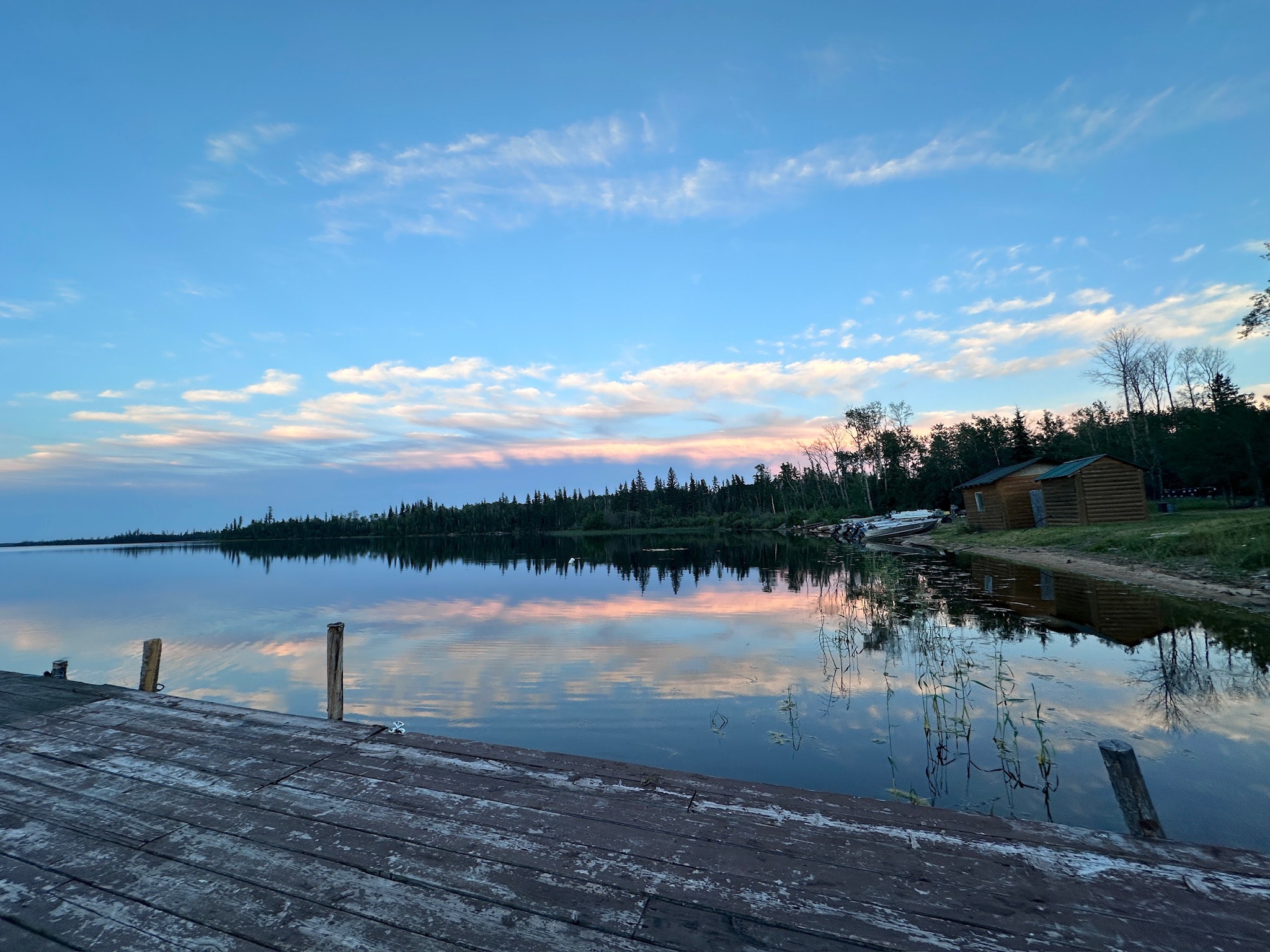 Lodge dock at dusk with boats moored and pastel pink clouds reflecting on the lake