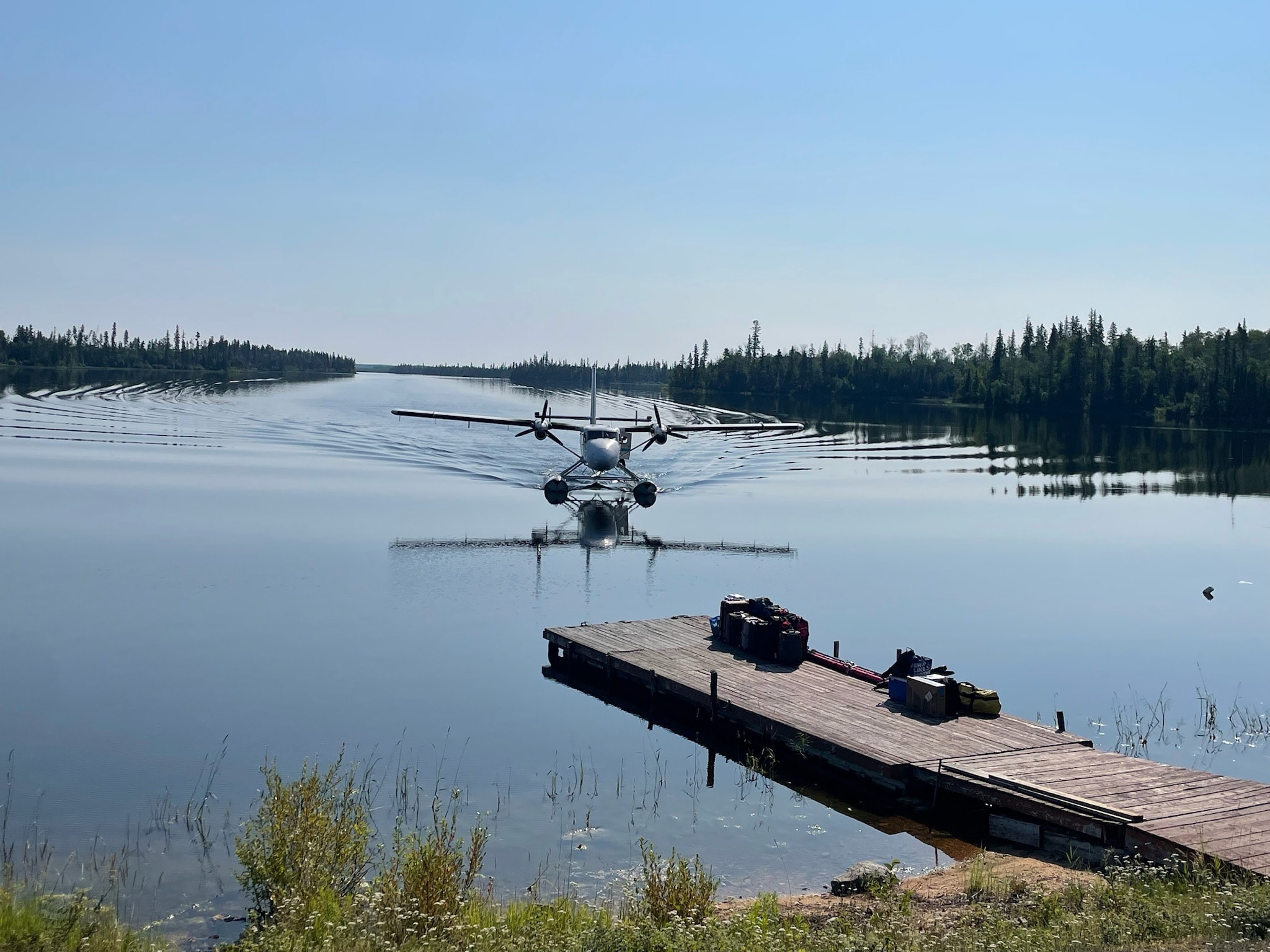 Twin Otter floatplane taxiing toward the dock with luggage waiting on the pier
