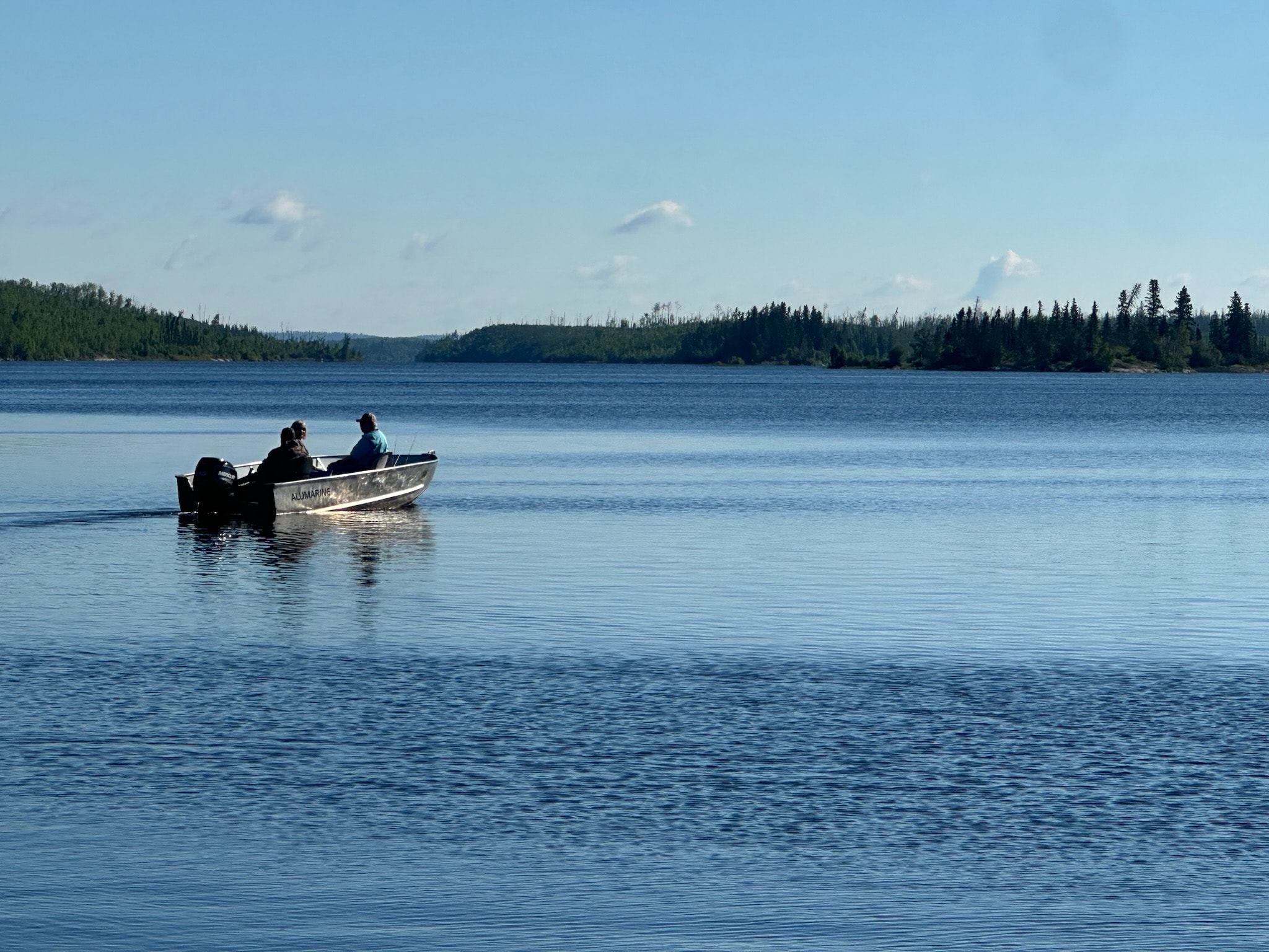 Two anglers in an aluminum fishing boat heading out on a calm wilderness lake