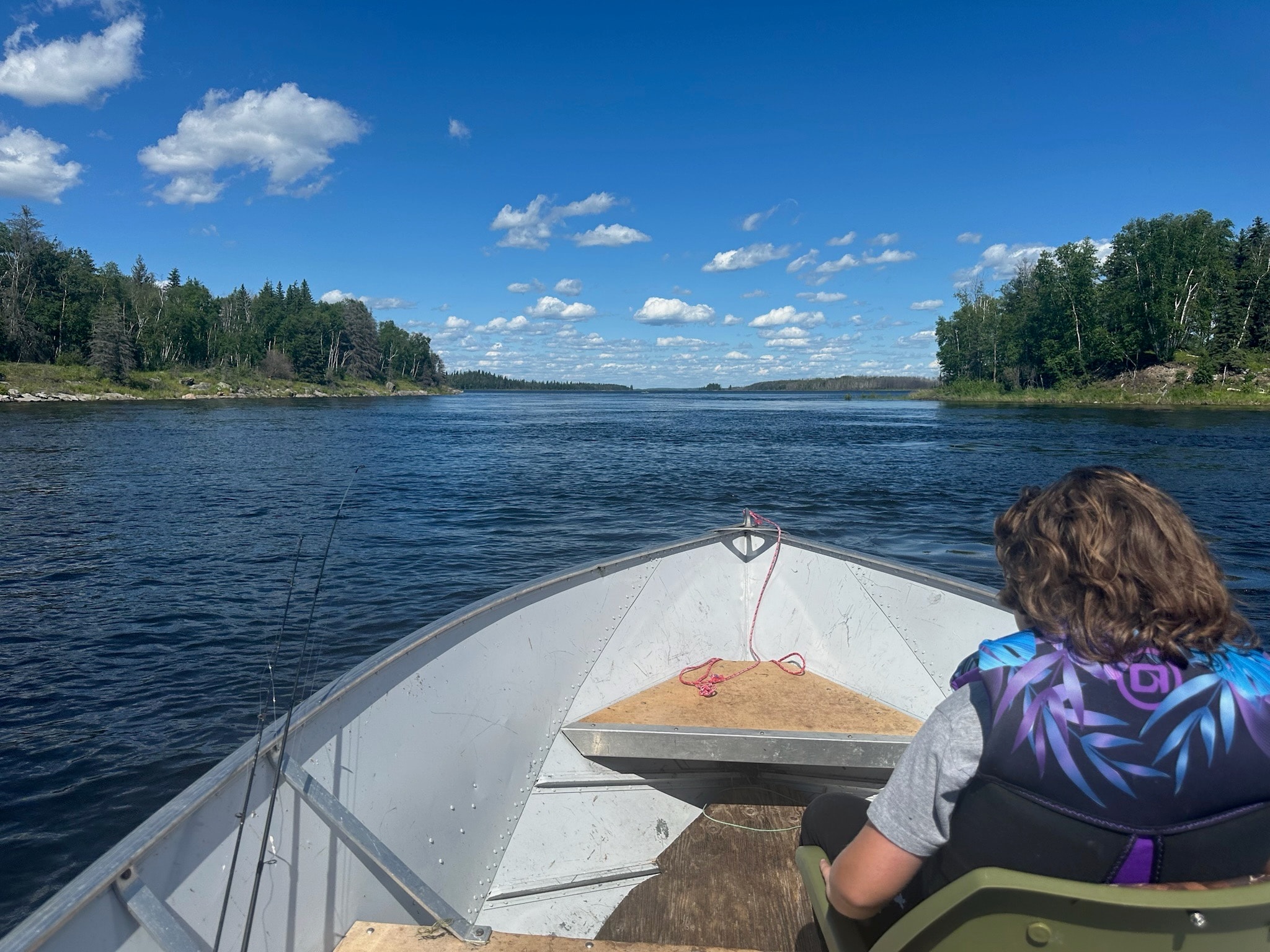 Child in life jacket riding in the bow of a fishing boat through a boreal river channel