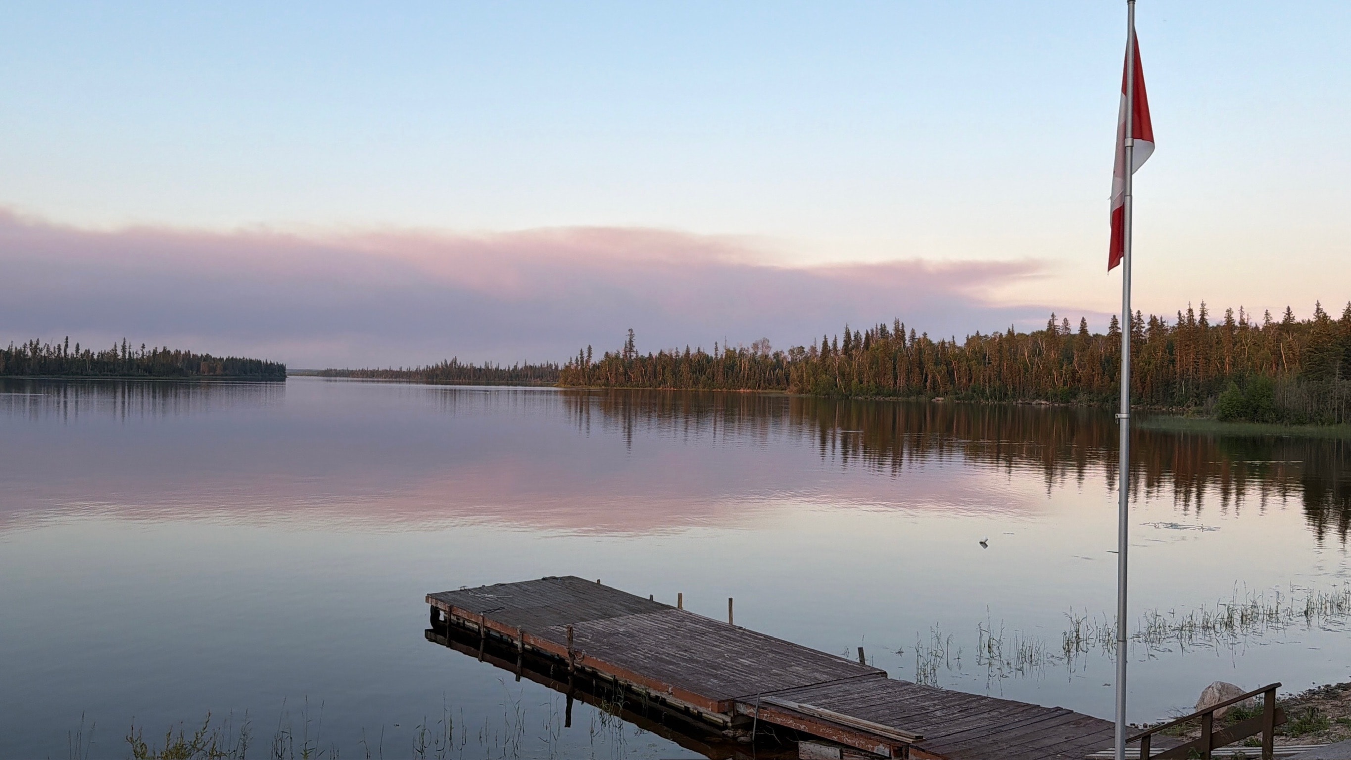 Canadian flag at the lodge dock at dusk with pink clouds reflecting on the calm lake