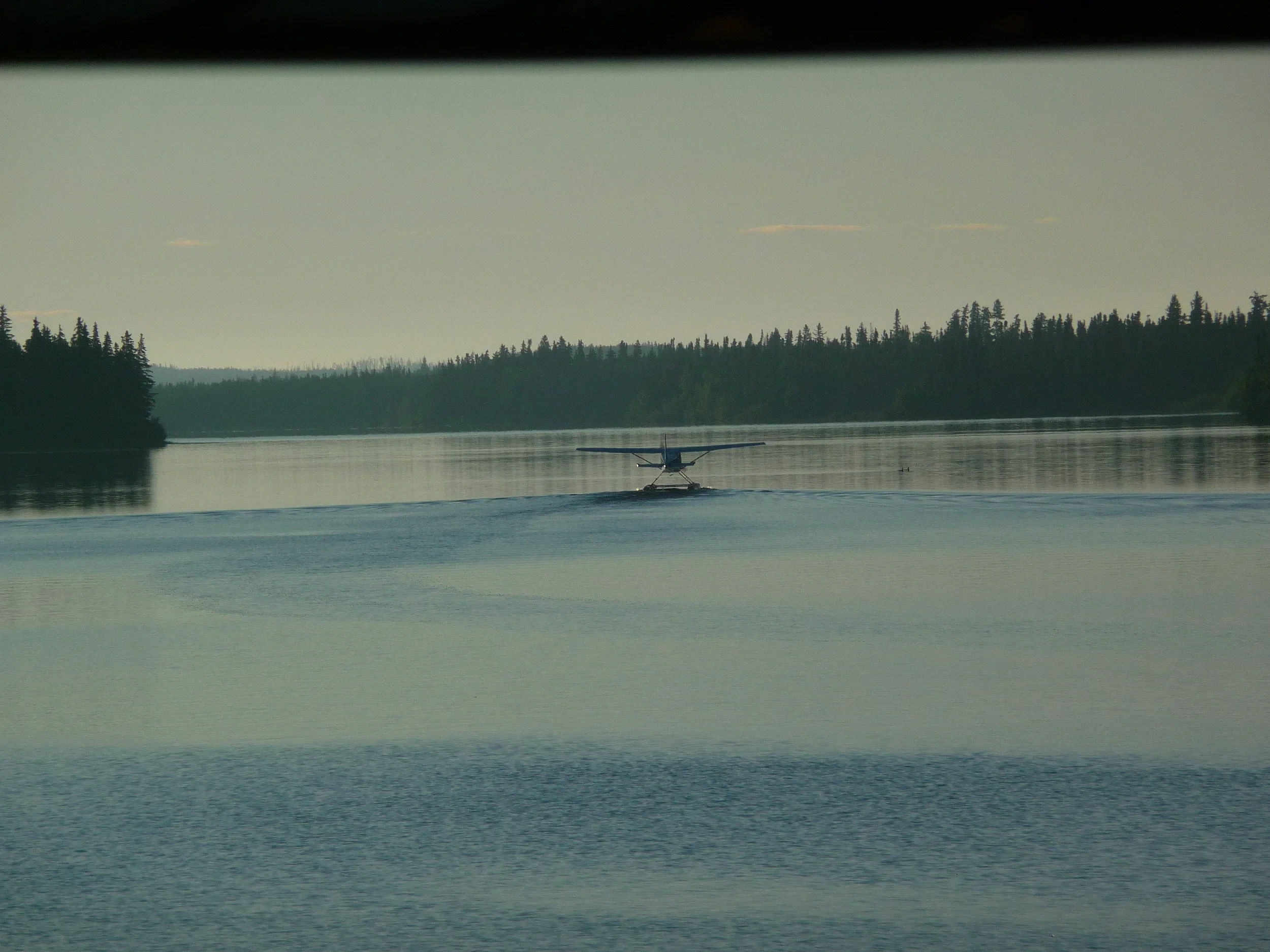 Floatplane taking off on a glassy wilderness lake at dusk